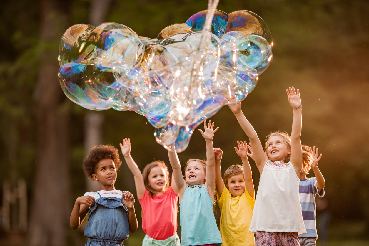 Group of happy kids having fun with heart shaped rainbow bubbles during a Bubble & Foam Party Rental with Mike's Trackless Trains