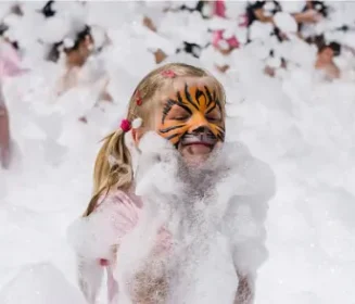 A little girl with face paint on, playing in foam, enjoying her Bubble & Foam Party Rental from Mike's Trackless Trains in Central Illinois
