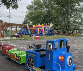 A trackless train car on a parking lot surface, next to a playground and bounce house, all courtesy of Mike's Trackless Trains